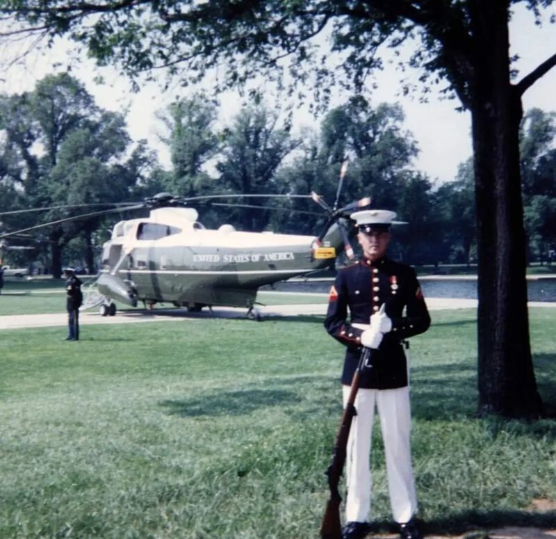 Travis McVey, dressed in his Marine Corps dress blues, stands in front of a military helicopter 